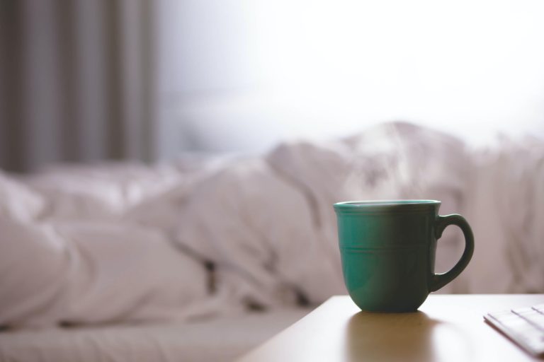 green mug with steam and white bed sheets in the background