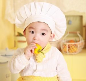 baby wearing chef costume eating a yellow bell pepper